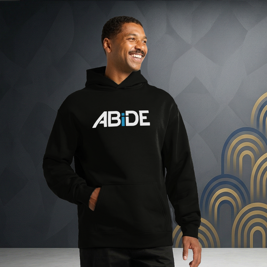 Man wearing a black hoodie with 'ABiDE' text against a geometric-patterned wall.