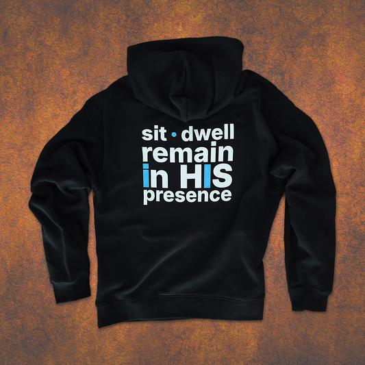 Black ABiDE hoodie with text 'sit dwell remain in HIS presence' on a textured brown background