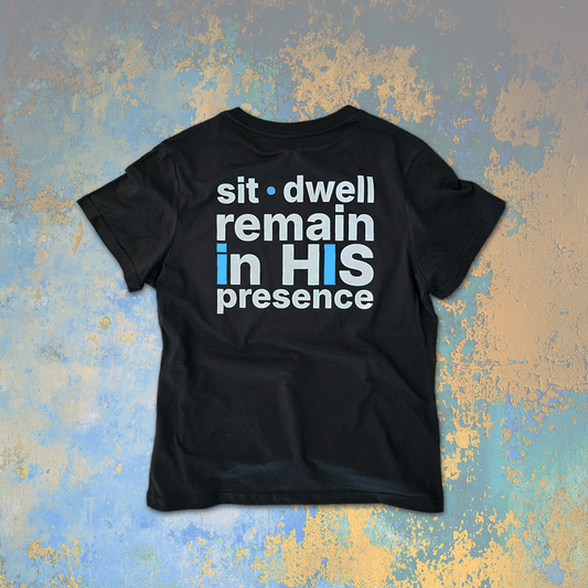 Dark gray women's t-shirt with sit dwell remain in HIS presence text on a textured blue and gold background
