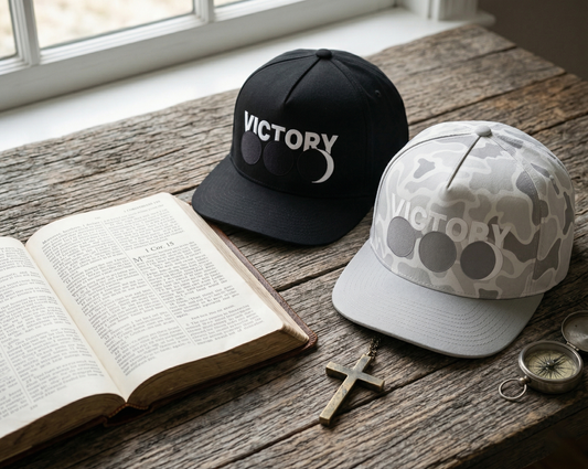 Two hats with 'VICTORY' branding on a wooden surface next to an open Bible.