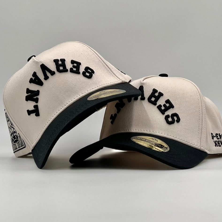 Two beige baseball caps with black 'SERVANT' text on a gray background