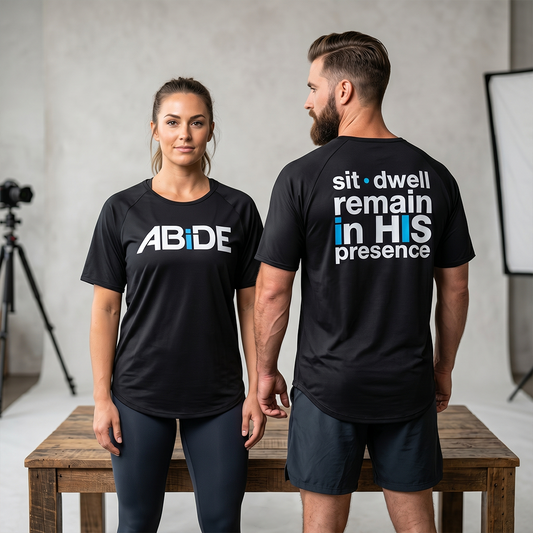 Man and woman wearing black bamboo t-shirts with ABiDE & sit dwell remain in HIS presence, one facing forward and the other facing backward.