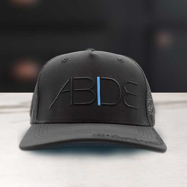 Black trucker cap with 'ABIDE' logo on a blurred background