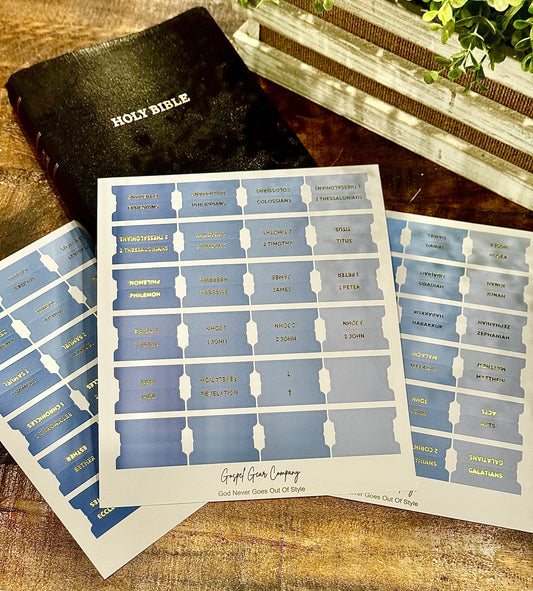 Sheet of blue and white labels with books of the Bible on a wooden surface next to a black Bible.