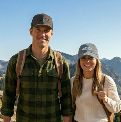 Two people wearing ABiDE hats with mountains in the background