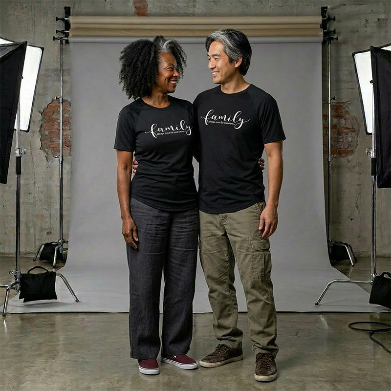 Two people wearing black t-shirts with 'Family - Always Room For One More' printed on them, standing in a studio setting.