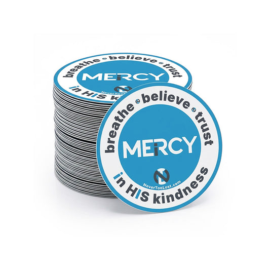 A stack of circular printed stickers with a grey, white, and blue design featuring the word 'MERCY' and the phrase 'breathe believe trust in HIS kindness'. One sticker is placed in front of the stack on a clean white background.