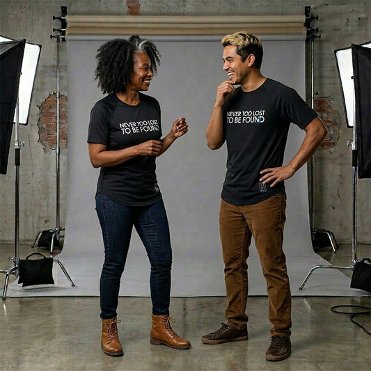 Two people wearing black t-shirts with Never Too Lost To Be Found text, standing in a studio setting.