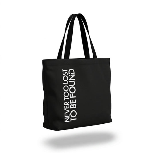 Black tote bag with white Never Too Lost To Be Found text on a white background