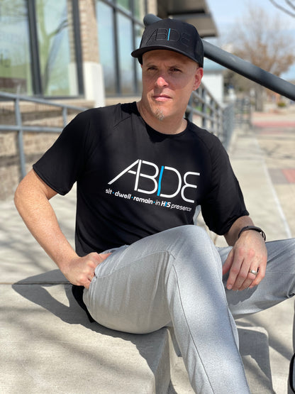 Now Found Co-Founder Steve Cohen sitting on stairs wearing ABIDE Black Trucker Hat and Black ABIDE sit - dwell - remain in His presence bamboo shirt