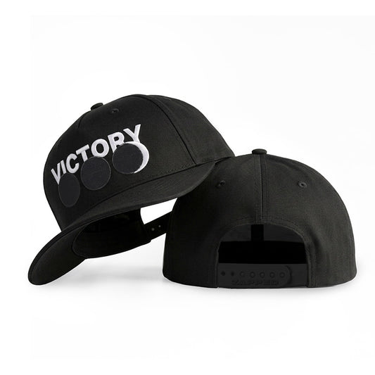 Two black snapback caps shown on a white studio background. The front cap displays a white 'VICTORY' logo with three circular cutouts on the front panel, and the back cap shows the adjustable snapback closure.