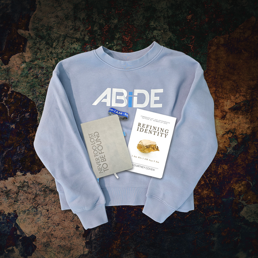 Light blue sweatshirt with 'ABIDE' text, placed on a textured surface with Refining Identity book, I am who I AM says I am bracelet  and Never Too Lost Journal