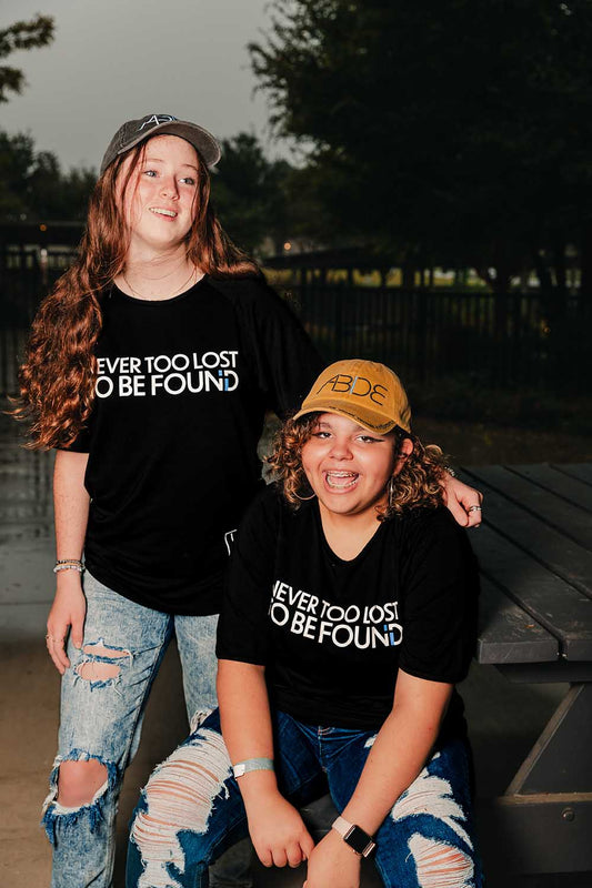 two youths, one in gray "abide" hat, the other in mustard yellow "abide" hat, wearing "never too lost" bamboo tees from now found apparel.
